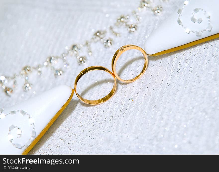 Two gold wedding rings standing together between bride's shoes