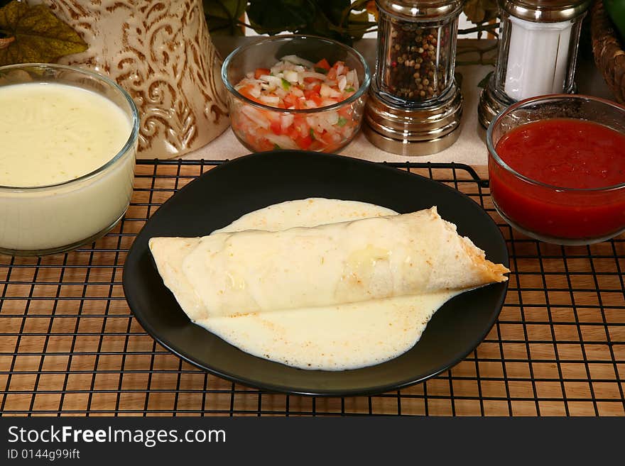 Chicken burrito in plate covered in cheese dip in kitchen or restaurant.