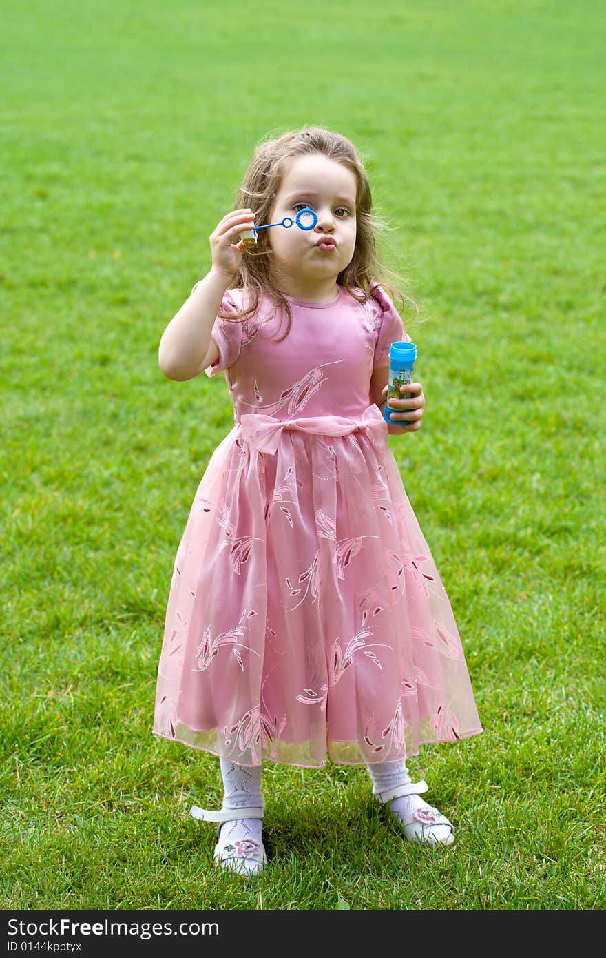 Little girl in pink dress is blowing bubbles on green grass. Little girl in pink dress is blowing bubbles on green grass