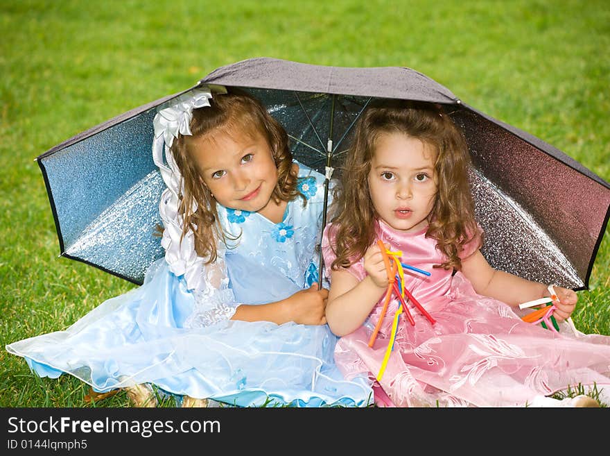 Two little girls are sitting under umbrella on green grass. Two little girls are sitting under umbrella on green grass