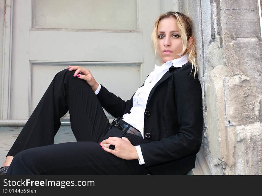 Pretty blond model dress with in a black suit sitting outside. Pretty blond model dress with in a black suit sitting outside