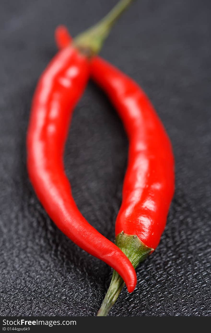 Two red chillies on black leather background, macro, shallow DOF