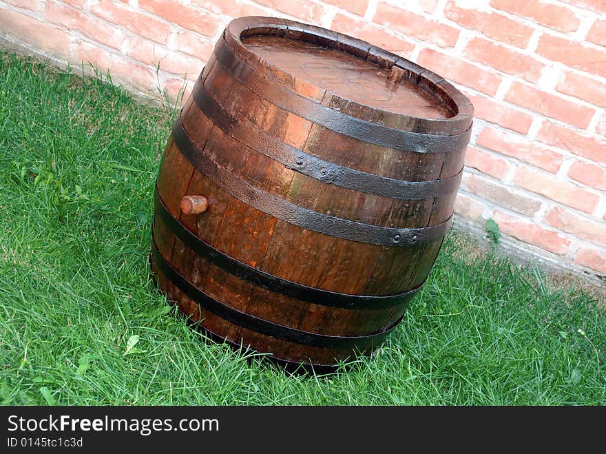 Old wooden wine brown barrel over grass and brick wall. Old wooden wine brown barrel over grass and brick wall