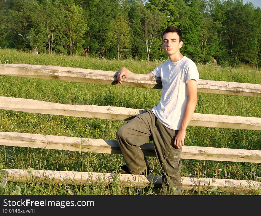 Young country boy leaning against a fence in a field. Young country boy leaning against a fence in a field.