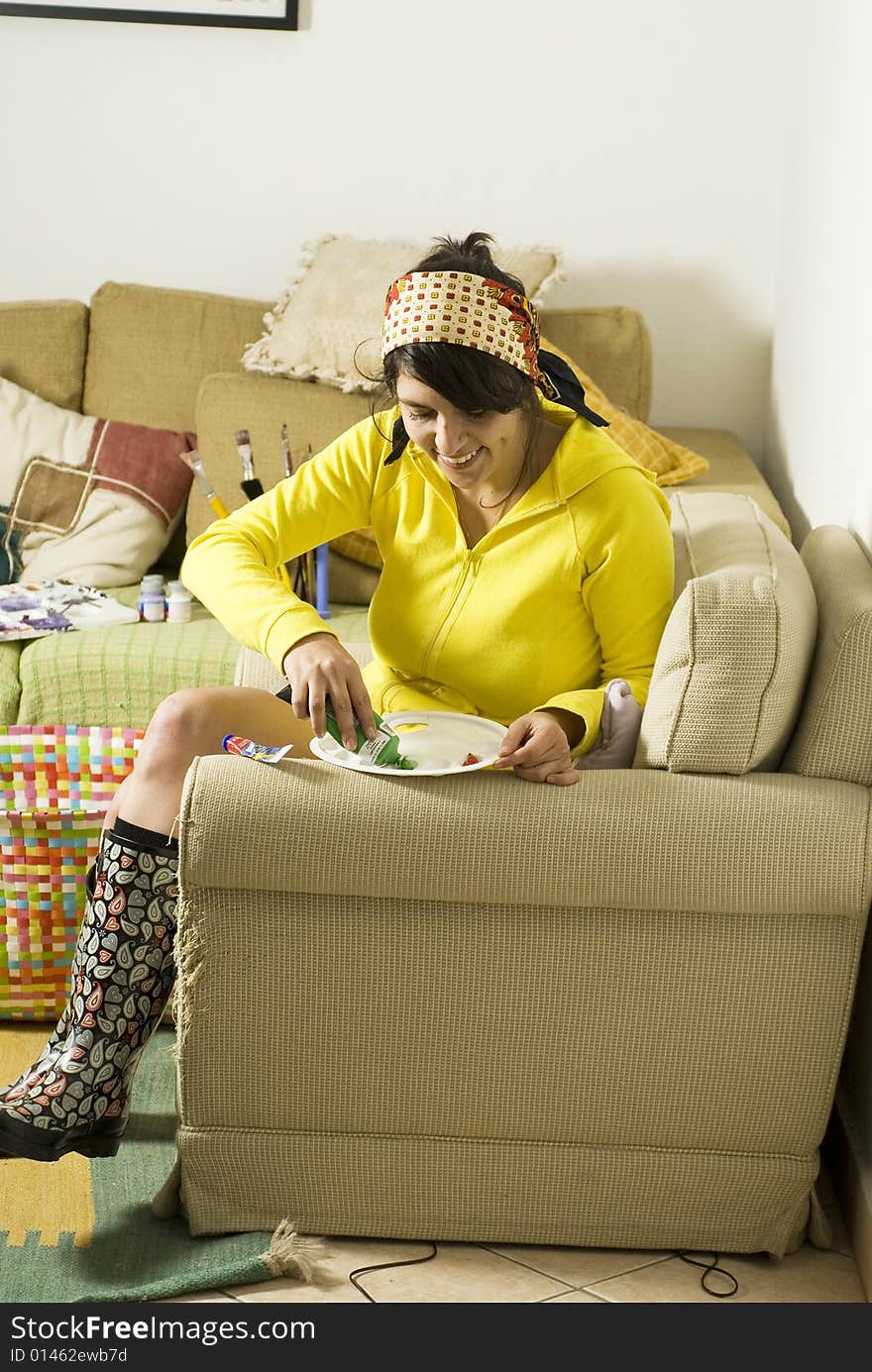 Female artist applying paint to palette while seated on her couch. Vertically framed photo. Female artist applying paint to palette while seated on her couch. Vertically framed photo.