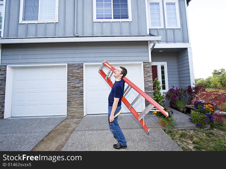 Laughing man standing in front of house holding ladder and hammer. Horizontally framed photo. Laughing man standing in front of house holding ladder and hammer. Horizontally framed photo.