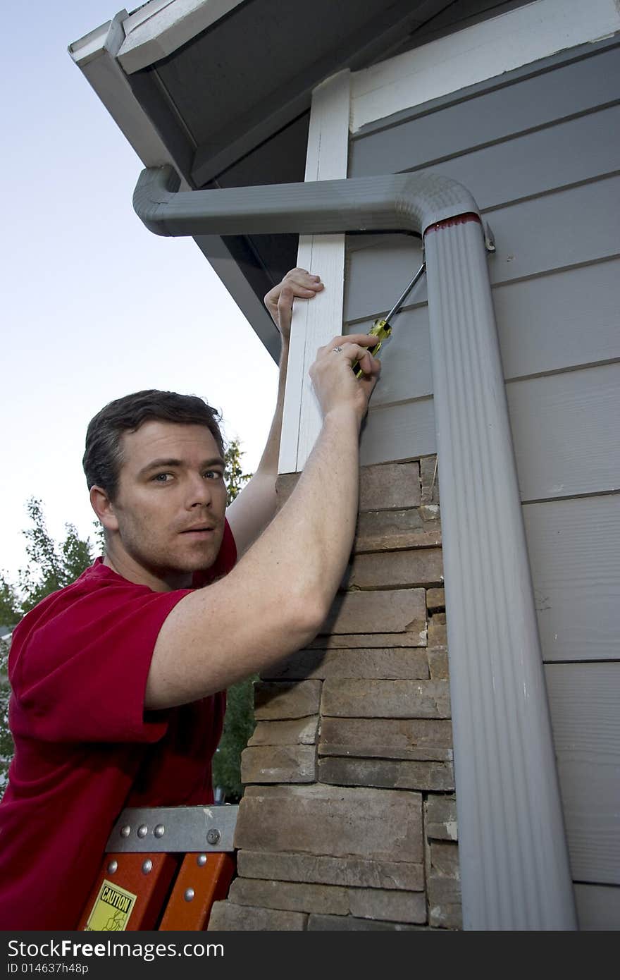 Man standing on a ladder fixing a house with a screwdriver. Vertically framed photo. Man standing on a ladder fixing a house with a screwdriver. Vertically framed photo.