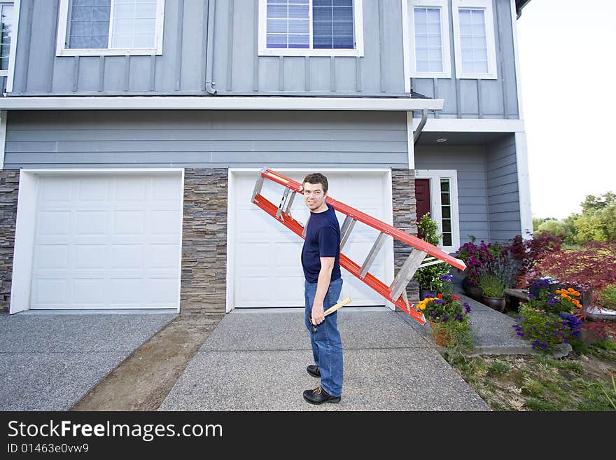 Smiling man standing in front of house holding ladder and hammer. Horizontally framed photo. Smiling man standing in front of house holding ladder and hammer. Horizontally framed photo.