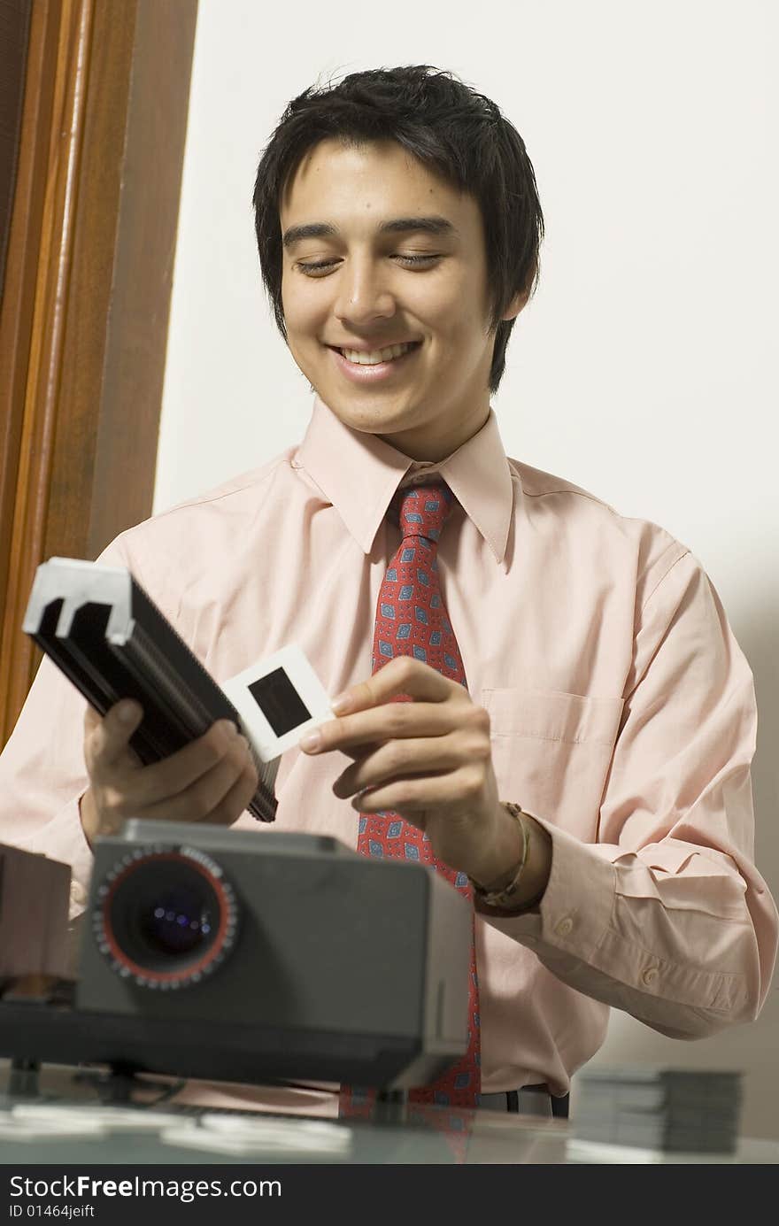 Man smiling as he looks at a slide next to a projector. Vertically framed photo. Man smiling as he looks at a slide next to a projector. Vertically framed photo.