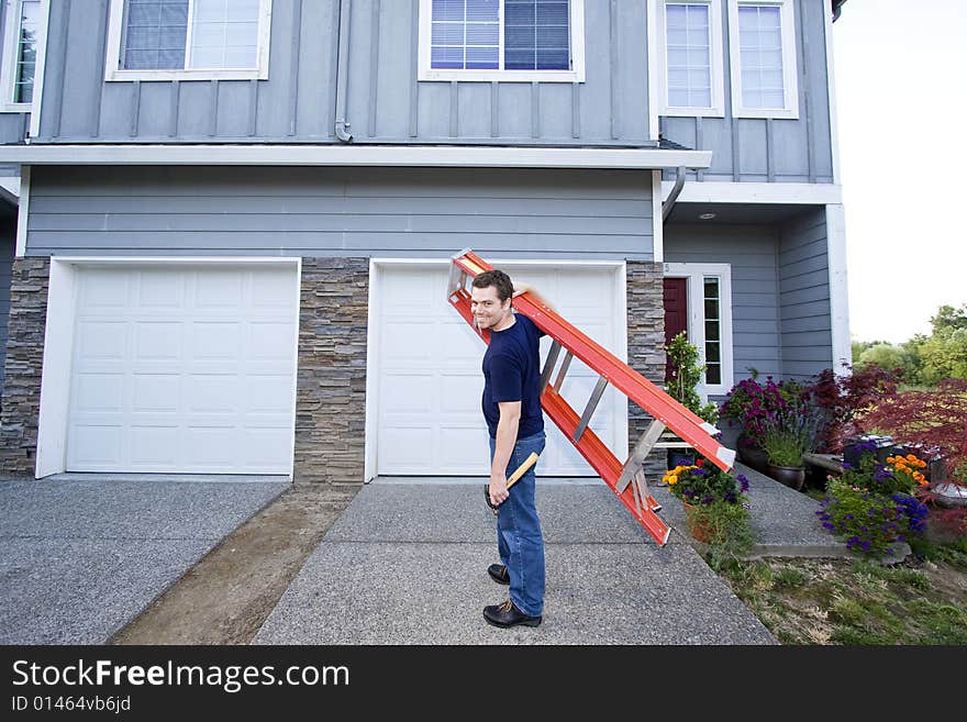 Smiling man standing in front of house holding ladder and hammer. Horizontally framed photo. Smiling man standing in front of house holding ladder and hammer. Horizontally framed photo.