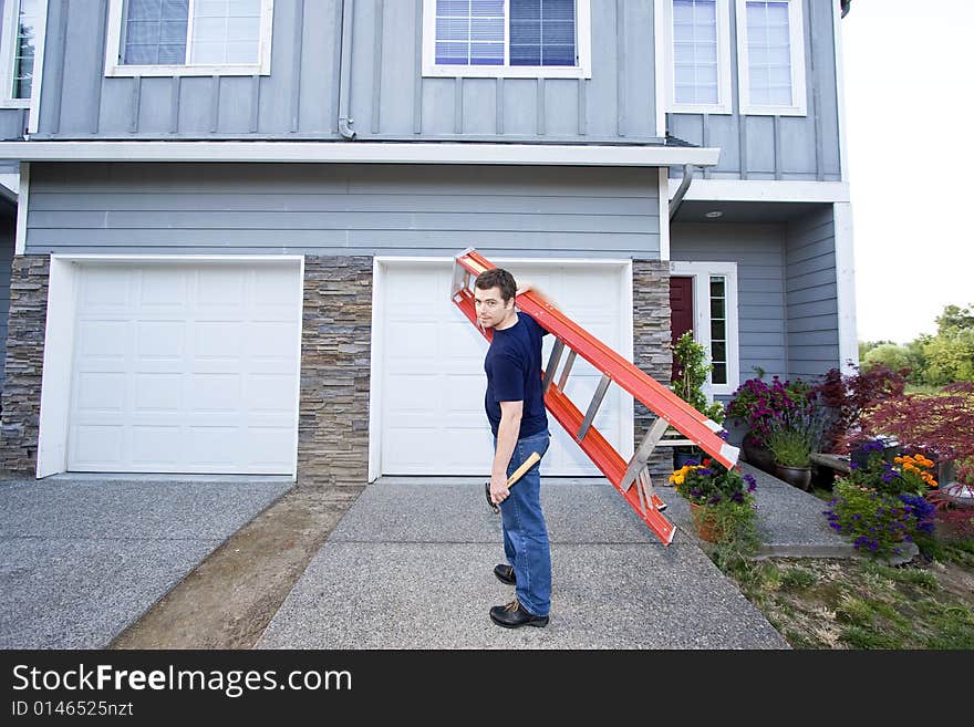 Man standing in front of house holding ladder and hammer. Horizontally framed photo. Man standing in front of house holding ladder and hammer. Horizontally framed photo.