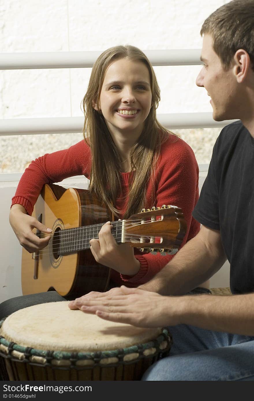 Woman playing guitar as she looks at the man next to her on the drums. Vertically framed photo. Woman playing guitar as she looks at the man next to her on the drums. Vertically framed photo.