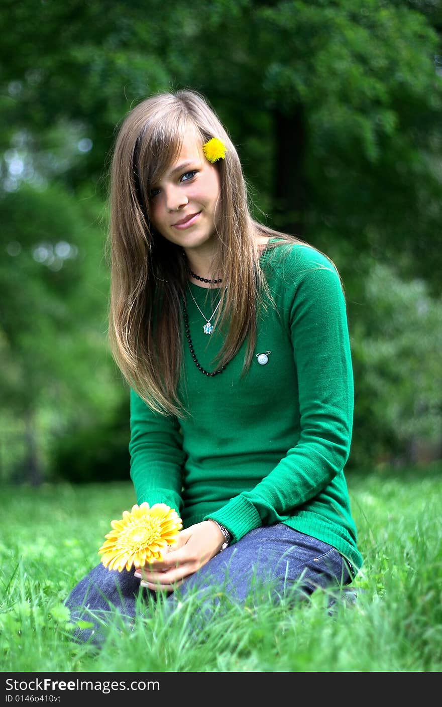 Photo presents a teenager on a grass holding a yellow flower. Photo presents a teenager on a grass holding a yellow flower