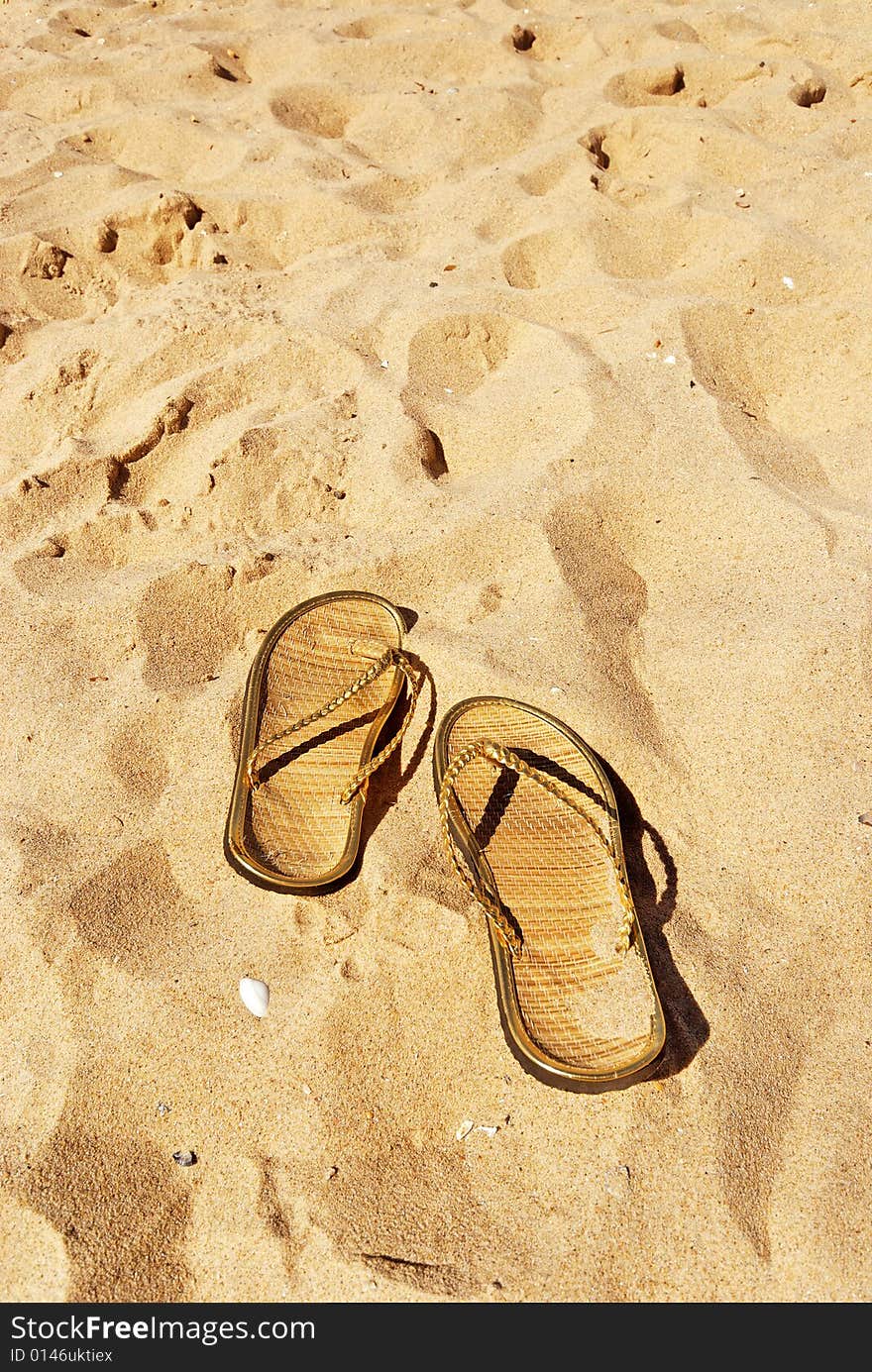 Pair of golden slippers left in the sand with shells. Pair of golden slippers left in the sand with shells