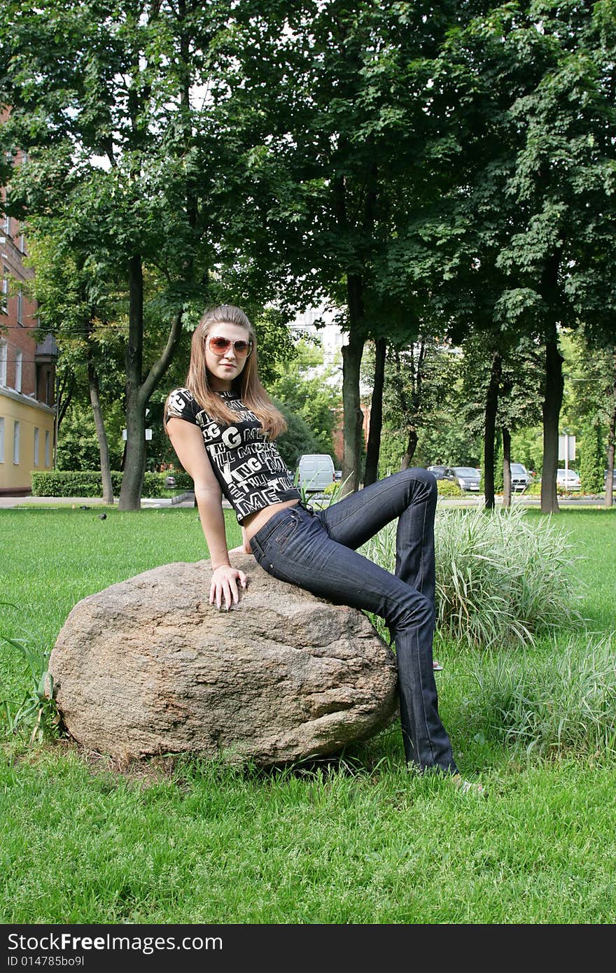 The fashionable girl sits on the big stone