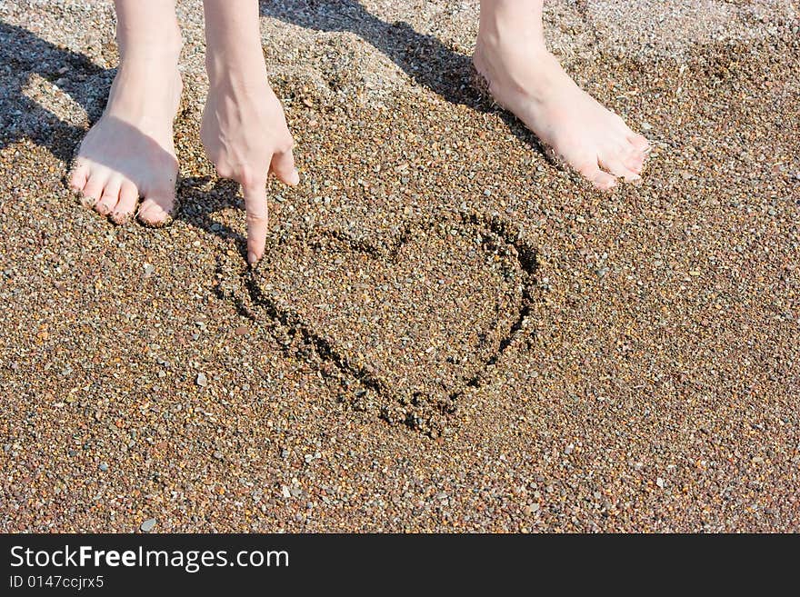 Painting heart on the wet sand on the beach.