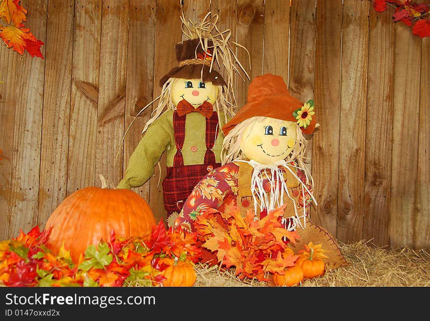 Happy scarecrows display, with pumpkin and fall leaves on straw bale. Room for text. Happy scarecrows display, with pumpkin and fall leaves on straw bale. Room for text.