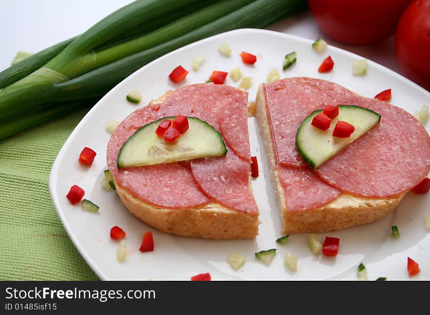 A breakfast of bread with sausage, cucumber and paprika