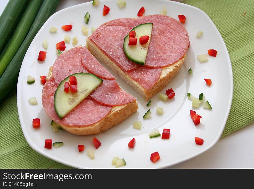 A breakfast of bread with sausage, cucumber and paprika