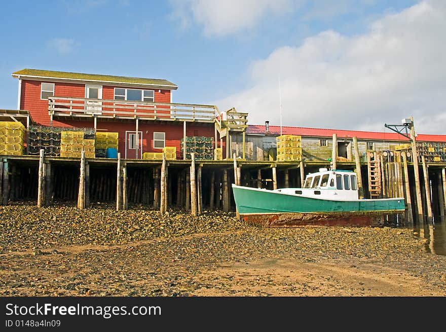 A view of a Maine lobster boat stuck and grounded at low tide next to a large fishing wharf or pier. A view of a Maine lobster boat stuck and grounded at low tide next to a large fishing wharf or pier.