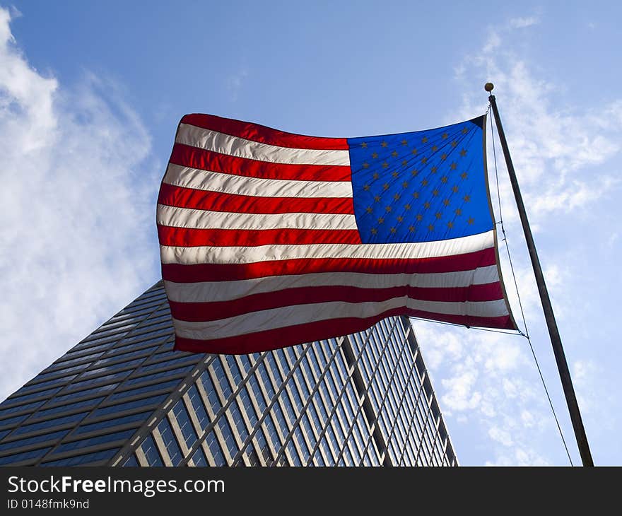 American flag waving against a skyscraper and a blue sky.