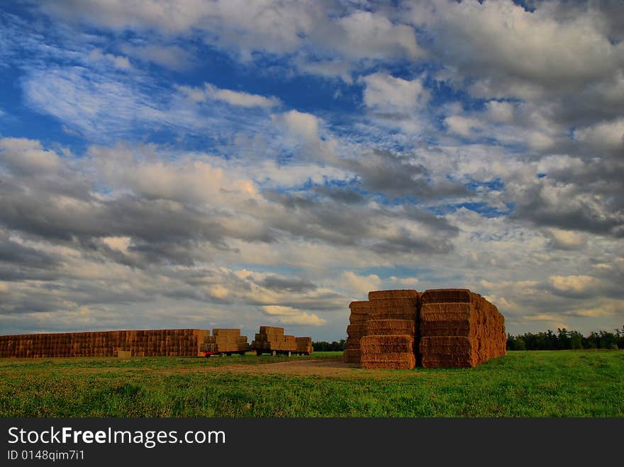 Walls of hay bales under cloudy summer skies. Two more flatbeds are ready to add to the pile. Walls of hay bales under cloudy summer skies. Two more flatbeds are ready to add to the pile.