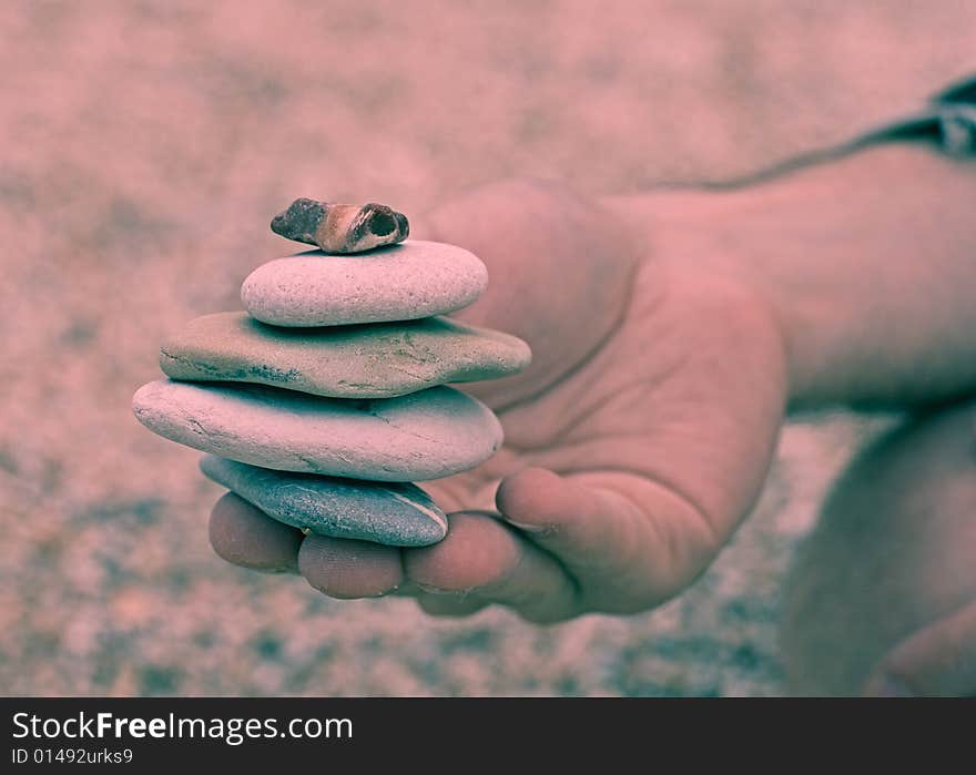 A stack of gray sandstones handed by someone on the seashore. The photo is cross processed