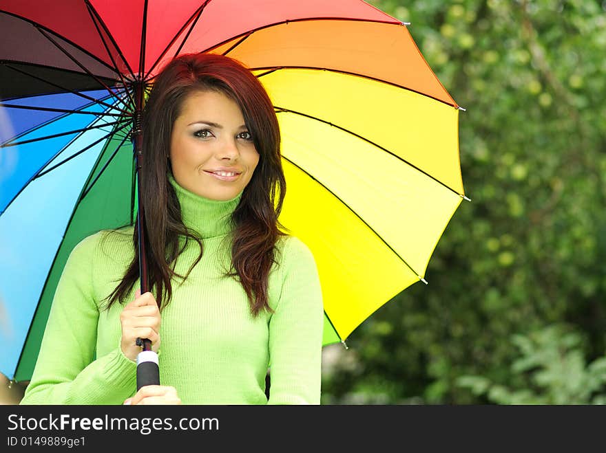 Beautiful woman under colorful umbrella relaxing in park. Beautiful woman under colorful umbrella relaxing in park