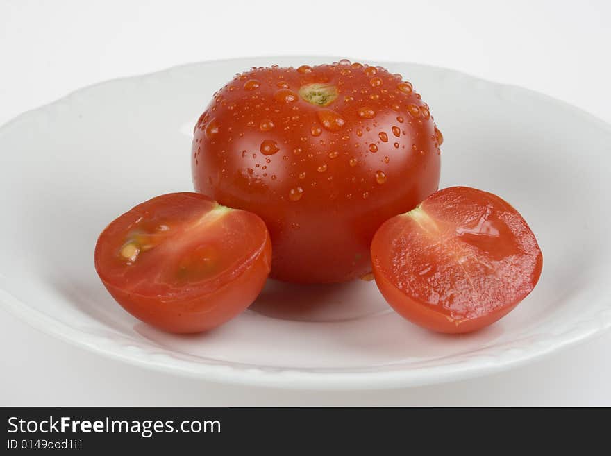 Whole tomato and sliced in two on white plate. Whole tomato and sliced in two on white plate