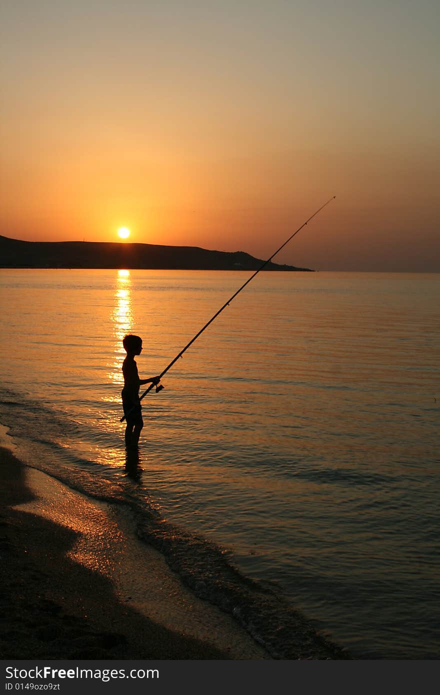 The silhouette of one fisherboy on the Sea of Azov against the background of the  sundown and mountains. The silhouette of one fisherboy on the Sea of Azov against the background of the  sundown and mountains.