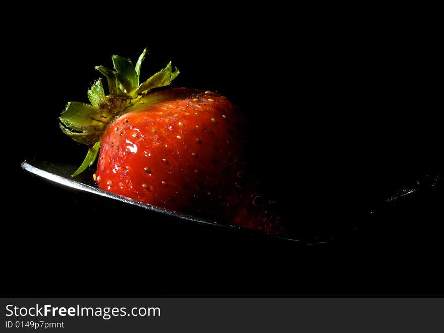 Strawberry sitting on spoon with strong flash from left, and isolated black background. Strawberry sitting on spoon with strong flash from left, and isolated black background