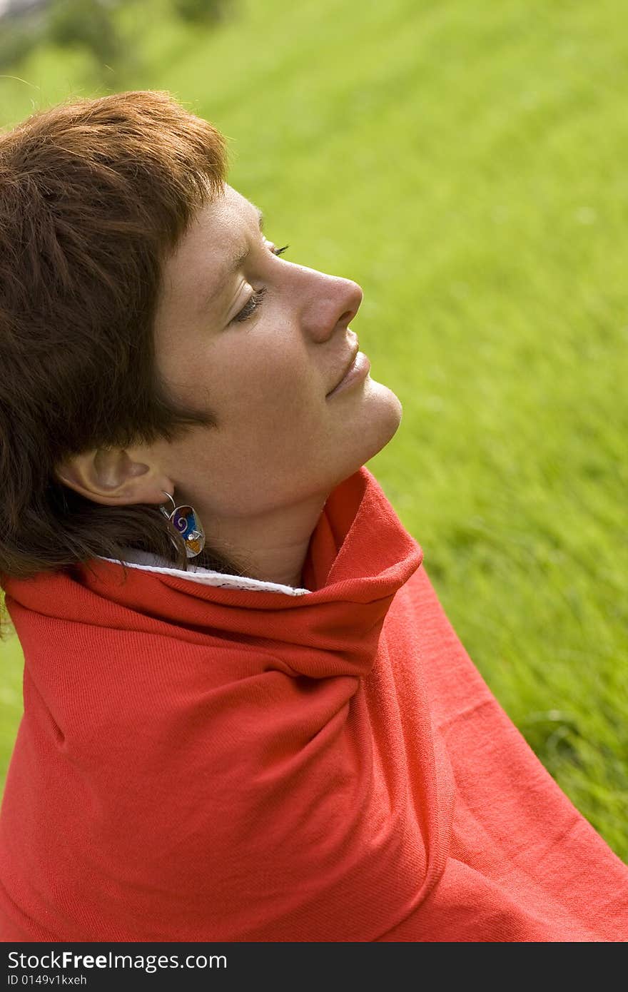 Closeup portrait of pretty redhead woman sitting on the grass