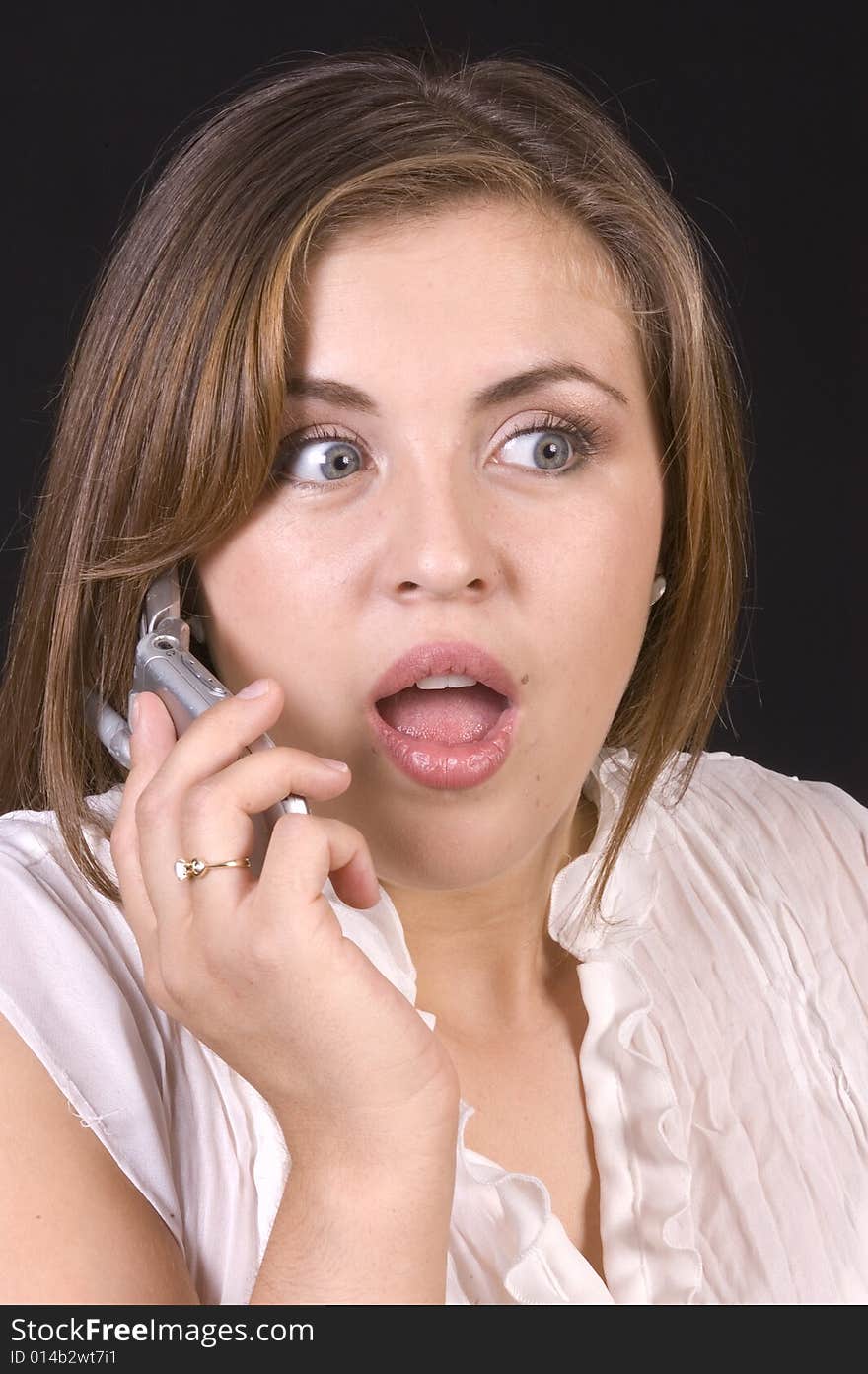 Pretty hispanic girl on a cell phone looking shocked over a black background