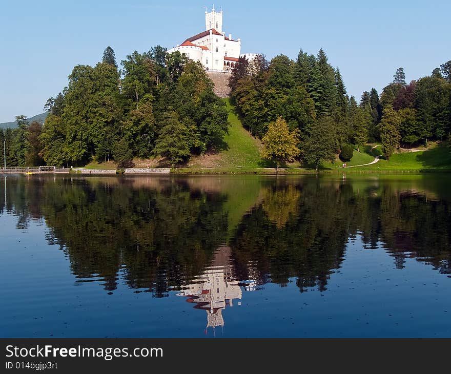 A castle on top of the hill surrounded with trees and lake