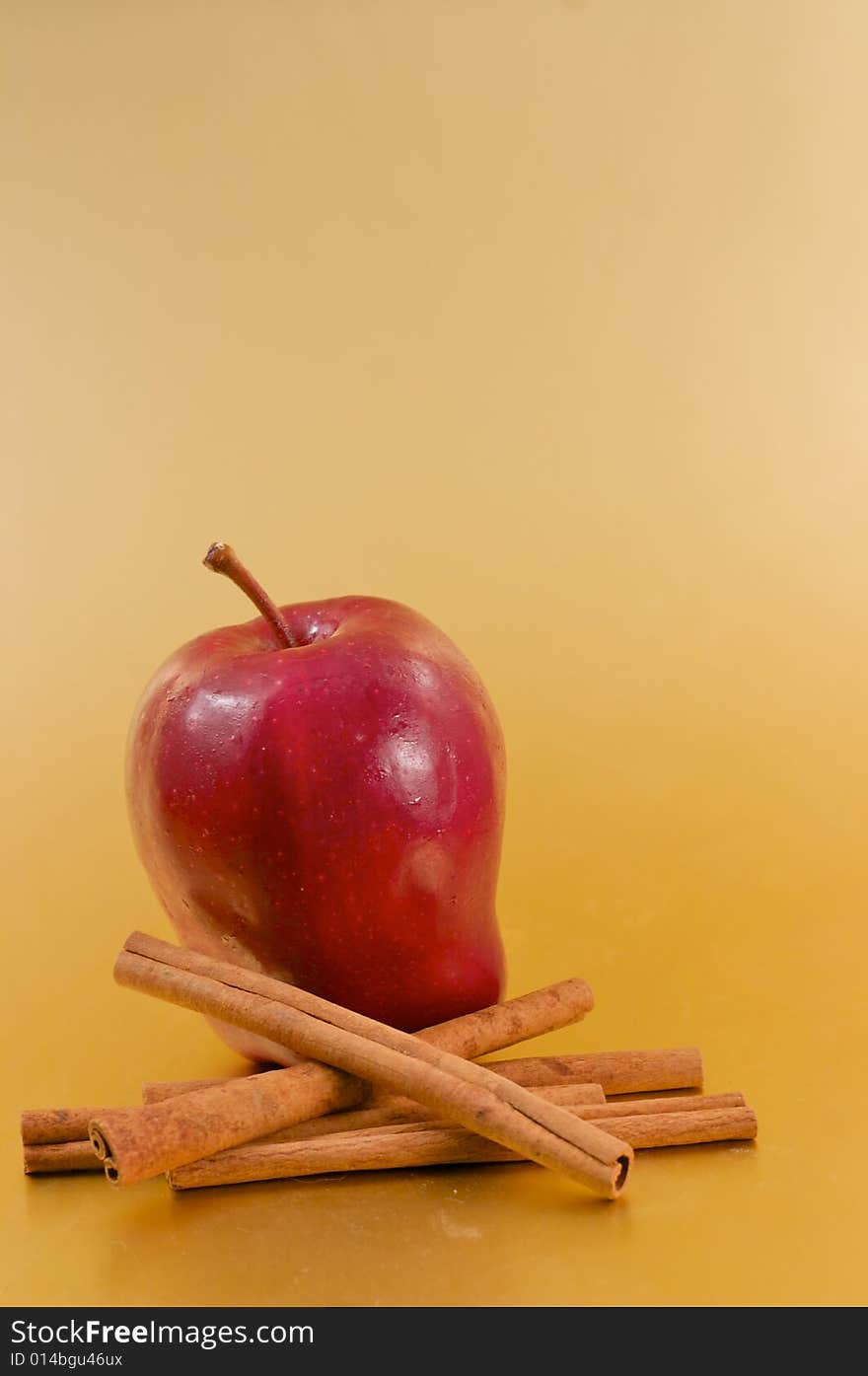 A red delicious apple with cinnamon sticks over a gold background