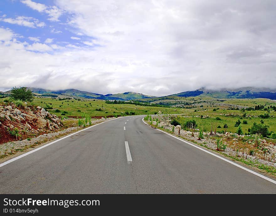 Gray road through mountain landscape under cloudy sky. Gray road through mountain landscape under cloudy sky