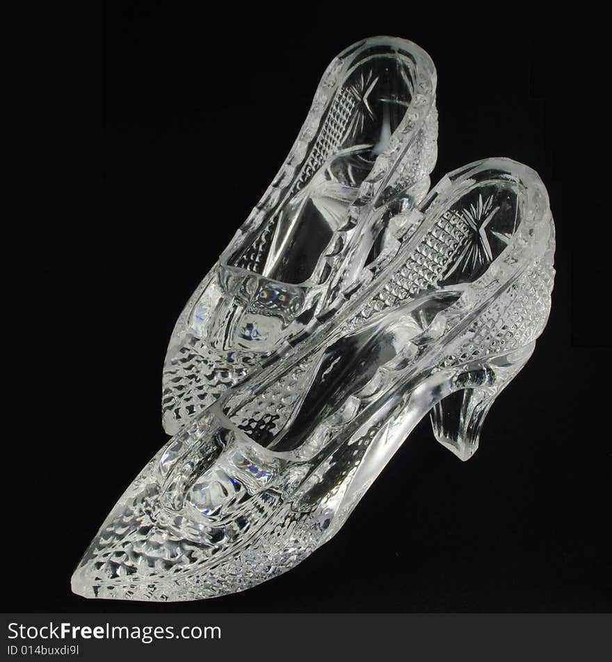 Two crystal glass slippers over black background