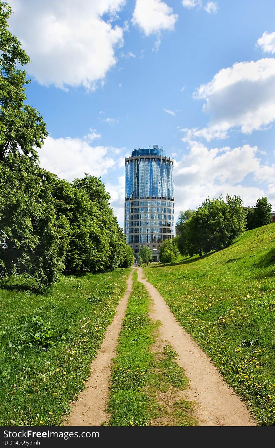 A dirt unsurfaced road contrasting with a modern-style highrise building. A dirt unsurfaced road contrasting with a modern-style highrise building