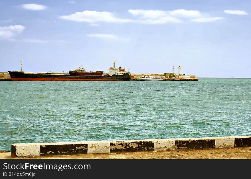 City Yalta. The peninsula of Crimea. Ukraine. Sunny day transport ship is far from the pier. Adjacent to the small boat. Even farther on the edge of the pier stands a lighthouse. City Yalta. The peninsula of Crimea. Ukraine. Sunny day transport ship is far from the pier. Adjacent to the small boat. Even farther on the edge of the pier stands a lighthouse.