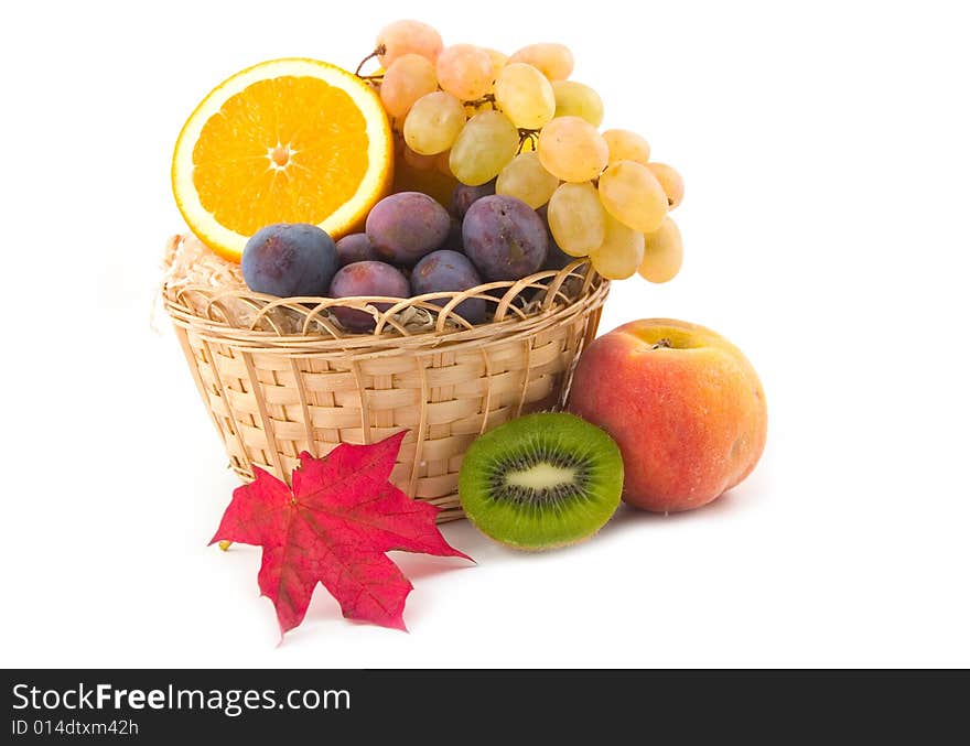 Red maple sheet and ripe fruit in a yellow basket on a white background