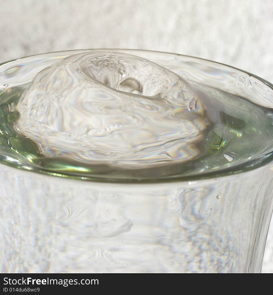 Droplets of water splashing into glass of water with resulting bulge in the meniscus, reflections and highlights. Droplets of water splashing into glass of water with resulting bulge in the meniscus, reflections and highlights