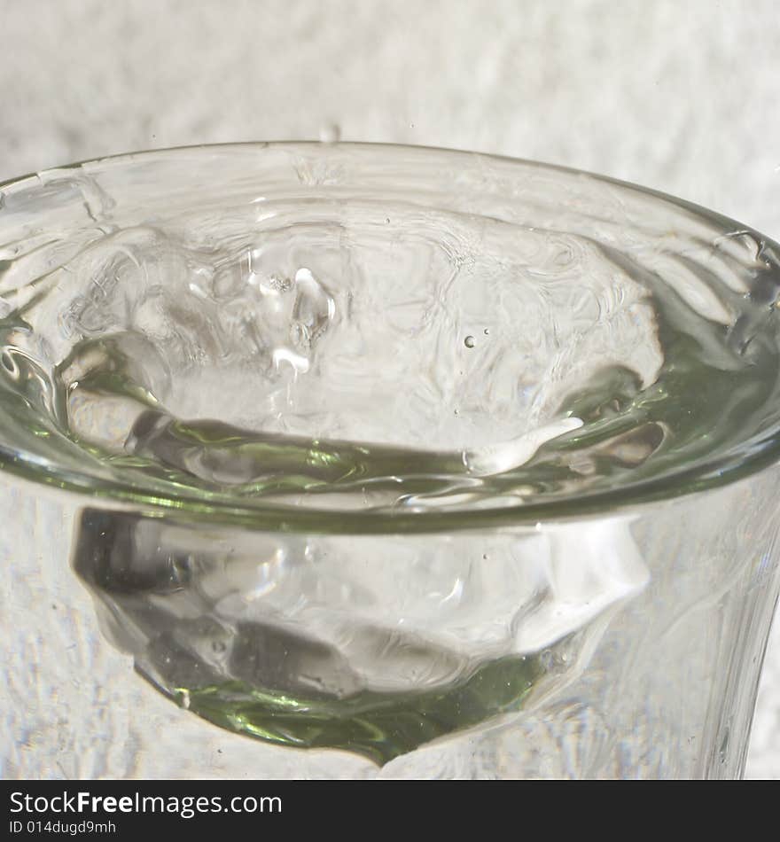 Droplets of water splashing into glass of water with resulting bulge in the meniscus, reflections and highlights. Droplets of water splashing into glass of water with resulting bulge in the meniscus, reflections and highlights