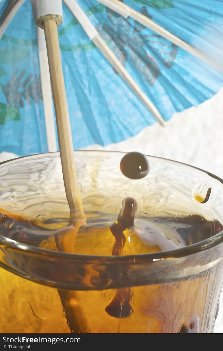 Droplet of rum falling towards glass of cola with cocktail umbrella with lovely specular highlights. Droplet of rum falling towards glass of cola with cocktail umbrella with lovely specular highlights