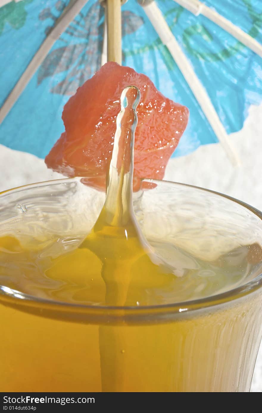 Droplet of spirit causing a splash as it enters the cocktail glass, with fruit garnish and cocktail umbrella. Droplet of spirit causing a splash as it enters the cocktail glass, with fruit garnish and cocktail umbrella