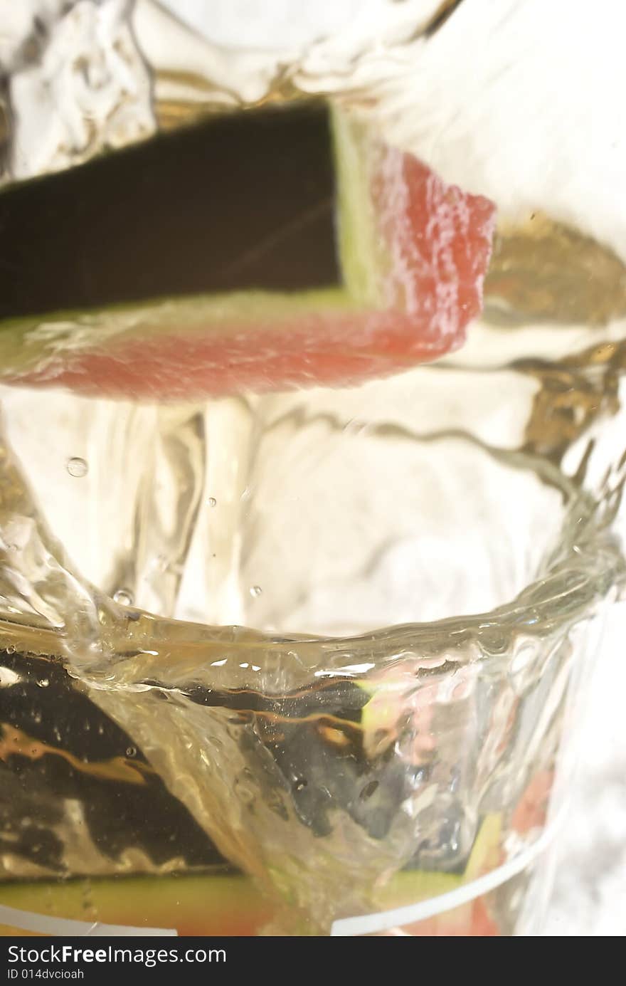 Piece of fruit causing a splash as it enters the cocktail glass, with bubbles, droplets and reflections. Piece of fruit causing a splash as it enters the cocktail glass, with bubbles, droplets and reflections