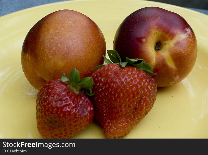 Two strawberries and two nectarines on a yellow plate. Two strawberries and two nectarines on a yellow plate