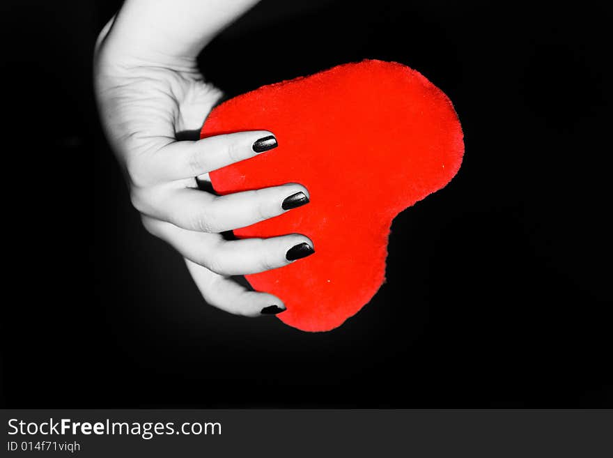 Brightly red heart in a female hand on a black background. Brightly red heart in a female hand on a black background