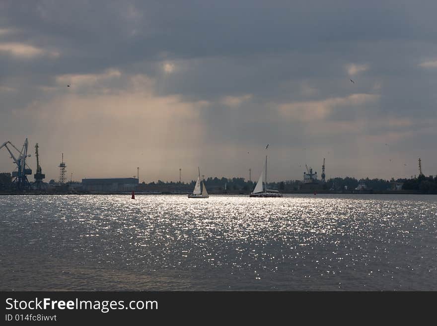 Two yachts on the river with birds flying around them and industrial view in the background. Two yachts on the river with birds flying around them and industrial view in the background