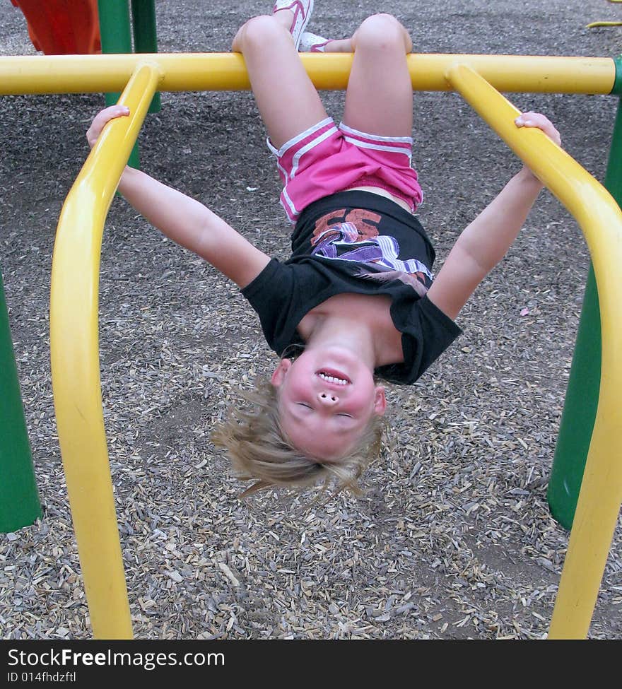 Little girl hangs upside down on the jungle gym at the playground. Little girl hangs upside down on the jungle gym at the playground.