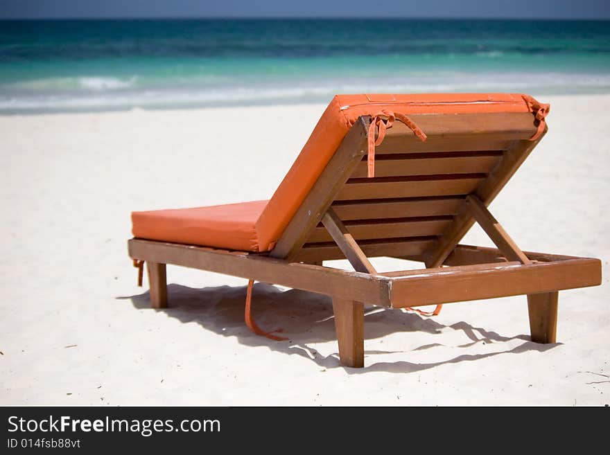 An orange bedchair facing the turquoise sea on a white sand beach. An orange bedchair facing the turquoise sea on a white sand beach